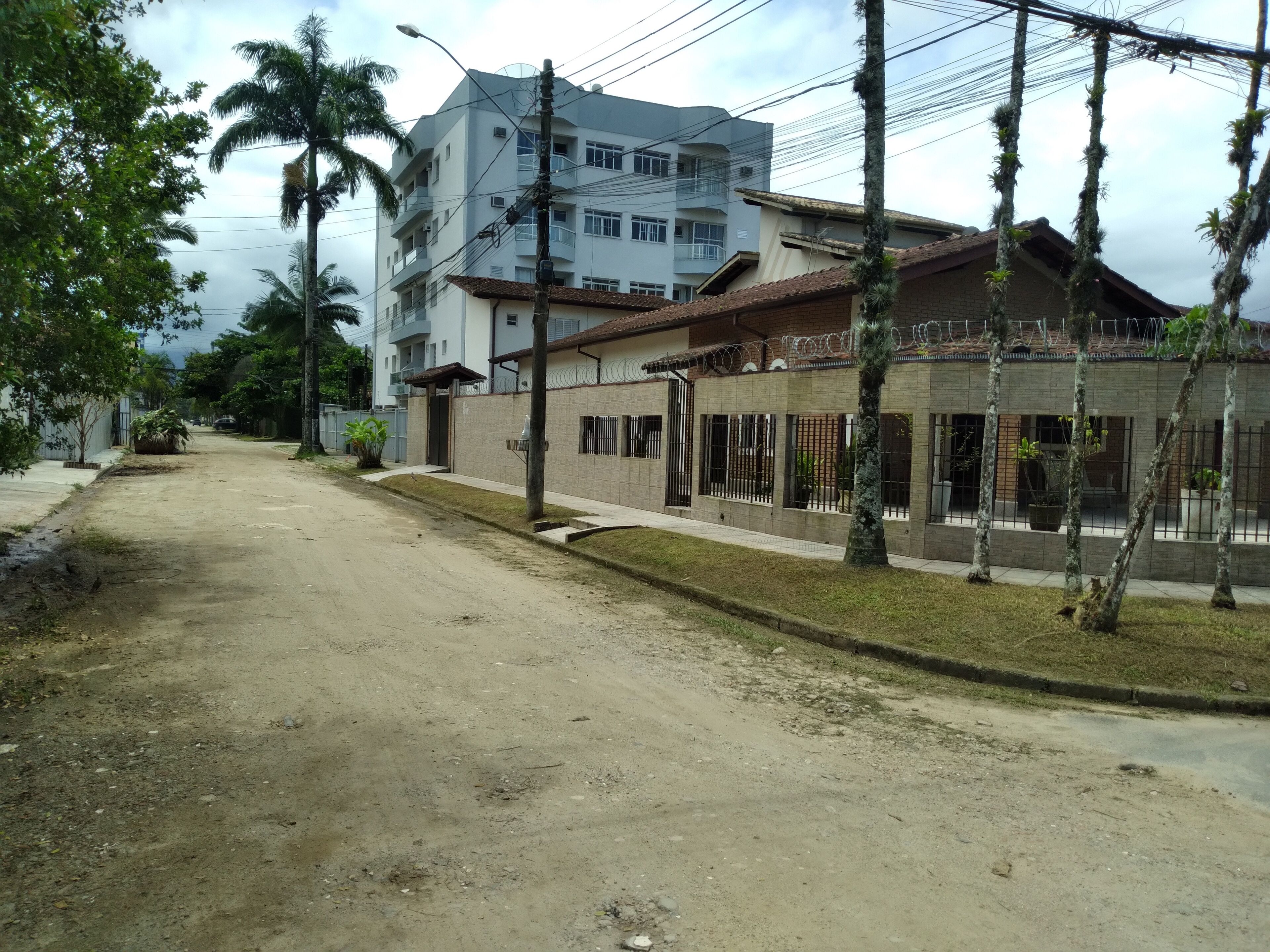 Une rue résidentielle bordée de maisons, avec un chemin de terre et, au fond, un immeuble à plusieurs étages.