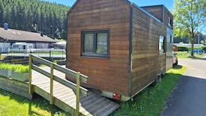 A small wooden cabin with a ramp leading to the entrance, surrounded by greenery and a clear sky. - Tiny House Prum - Natururlaub in der Eifel (Pruem)