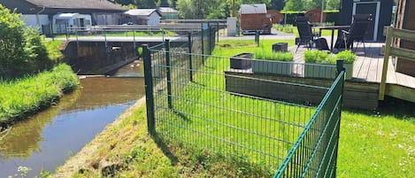 Un espacio al aire libre con valla, un río, construcciones de madera y un puente.