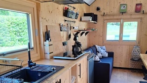 A compact kitchen with a sink, stove, and cabinets, a small dining area with a table and chairs, and a sofa. - Tiny House Prum - Natururlaub in der Eifel (Pruem)
