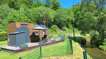 Eine moderne Holzhütte mit einer Terrasse, Solaranlagen und Blick auf einen Fluss.