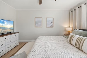 Ein Schlafzimmer mit einem Bett, einem Fernseher, einer Kommode, zwei gerahmten Bildern und einer Lampe.