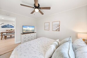 Een slaapkamer met een bed, een plafondventilator, een televisie op een dressoir en kunst aan de muur.