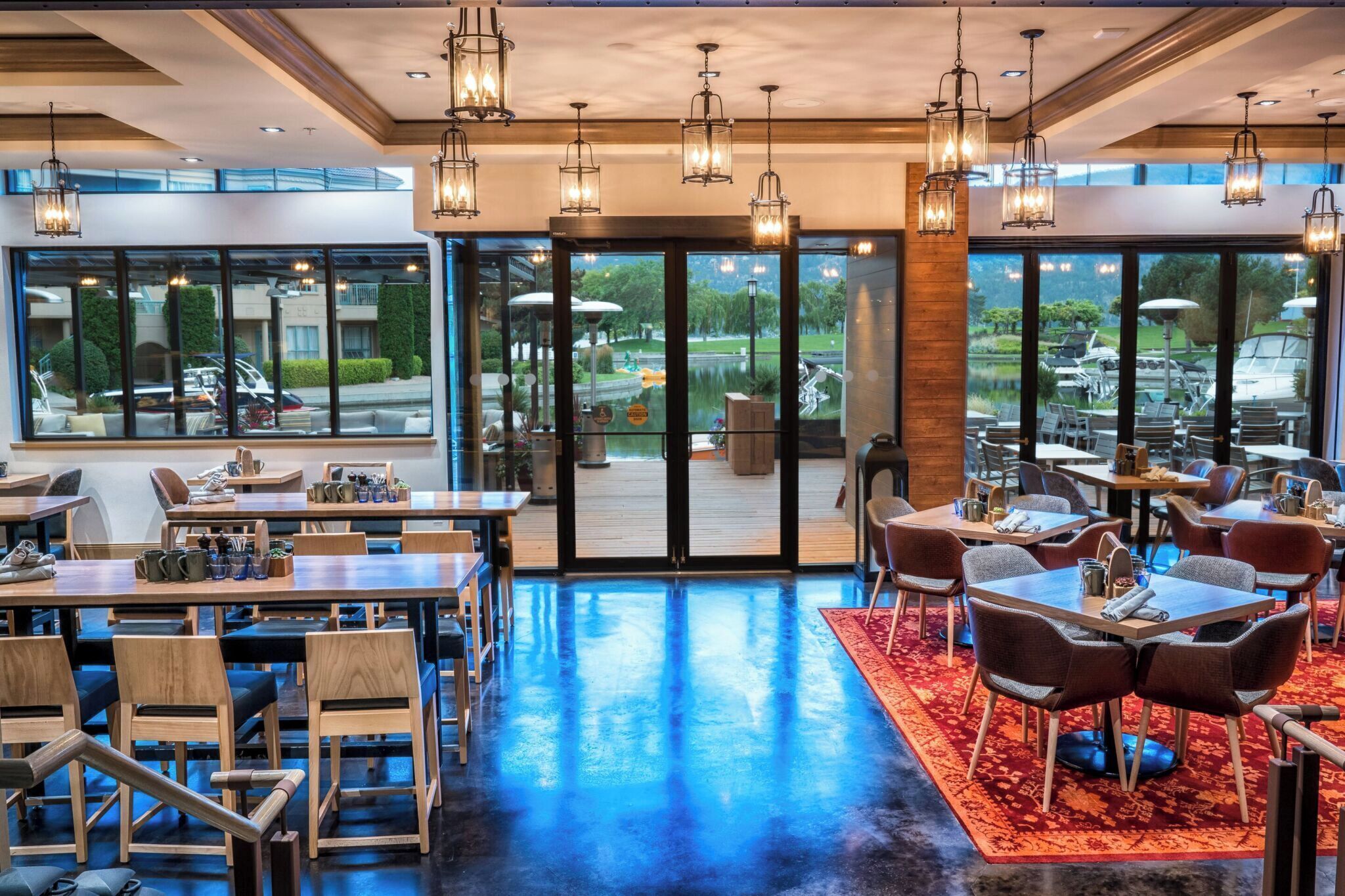 A spacious indoor area with tables and chairs, large windows, and hanging lights.