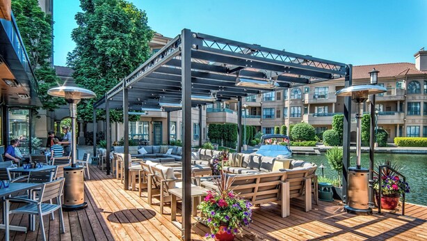 Terraza de madera con mobiliario exterior, un espacio cubierto y vista a un cuerpo de agua.