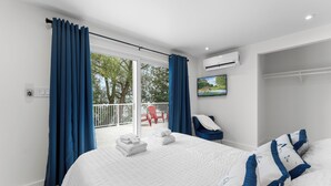 Un dormitorio con cama, televisión, aire acondicionado y balcón con silla y toallas.