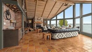 Amplia sala de estar con chimenea, ventanas grandes con vistas a un cuerpo de agua y una zona de estar acogedora.
