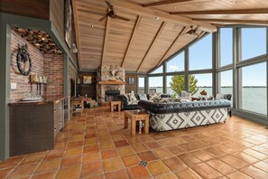 A spacious living area with a fireplace, large windows overlooking a body of water, and a cozy seating arrangement. - Your Private Waterfront Luxury, Leisure & Comfort! (Frontenac Islands)