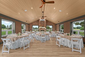 A spacious indoor dining area with multiple round tables, white chairs, and a brick wall backdrop.