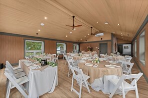 A spacious dining area with multiple round tables, white chairs, and a ceiling fan. - Your Private Waterfront Luxury, Leisure & Comfort! (Frontenac Islands)