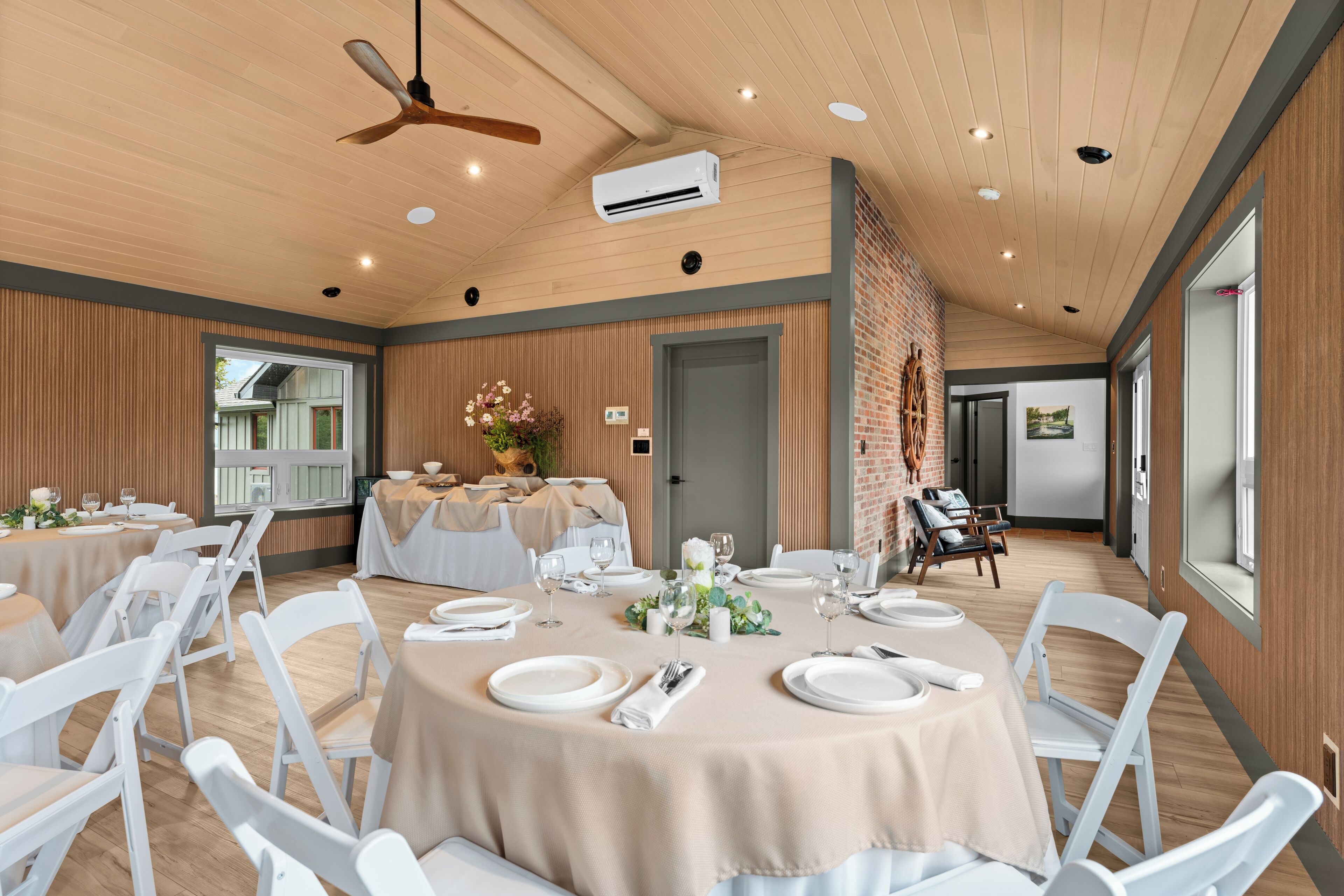 A spacious dining area with round tables, white chairs, and a ceiling fan.