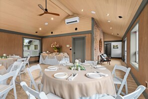 A spacious dining area with round tables, white chairs, and a ceiling fan.