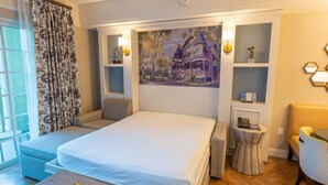 Et hotelværelse med seng, siddeplads, kunst og et skrivebord med lampe.