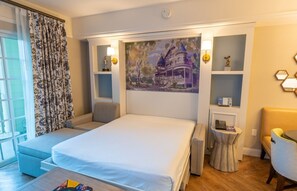 Una habitación de hotel con cama, zona de estar, obras de arte y un escritorio con lámpara.