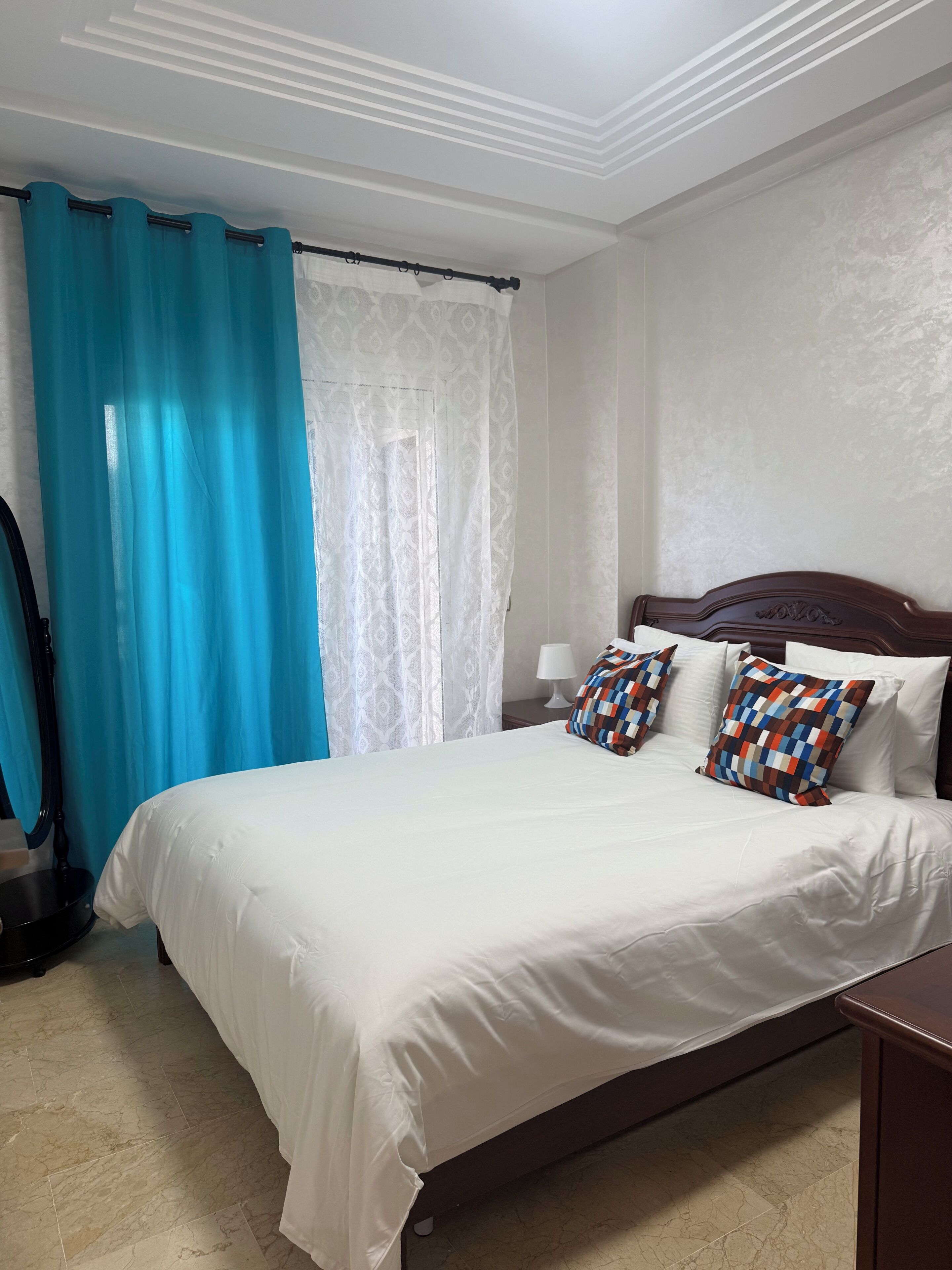 A hotel room with a bed, a nightstand, a lamp, and a window with curtains.