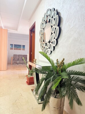 A hallway with a decorative mirror, potted plants, and a glimpse of a dining area in the background. - Bright apartment with a pool, 5-minute walk to the beach (Témara)