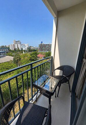 Ein Balkon mit einem Glastisch und zwei Korbstühlen, mit Blick auf eine Stadtlandschaft aus Gebäuden und Grünflächen.