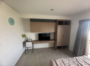Ein modernes Schlafzimmer mit einem Bett, einem Fernseher auf einem Holzständer, einem Schreibtisch mit Stuhl und einem Kleiderschrank.