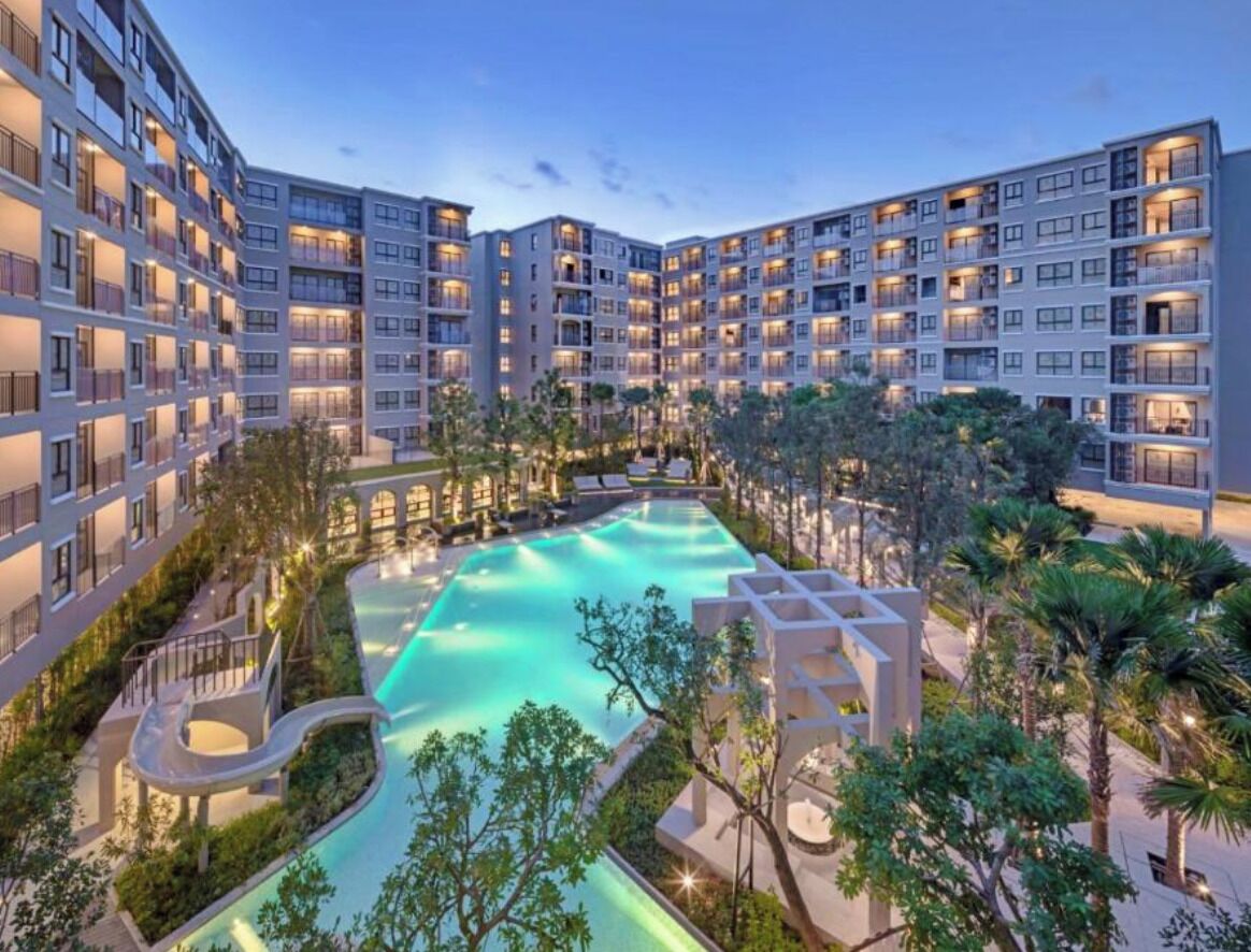 Ein mehrstöckiges Hotel mit einem zentral gelegenen Schwimmbecken, umgeben von Grünflächen und Palmen.