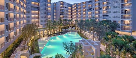 A multi-story hotel with a central swimming pool surrounded by greenery and palm trees.