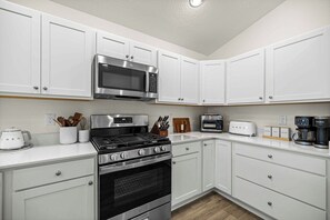 A kitchen with white cabinets, a stainless steel stove, a microwave, a toaster, and a coffee maker. - Dog-Friendly Coastal Cottage | Golf Cart (Sumterville)