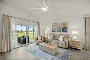 A spacious living room with a large sliding glass door leading to a patio, a ceiling fan, and a view of the outdoors. - Dog-Friendly Coastal Cottage | Golf Cart (Sumterville)