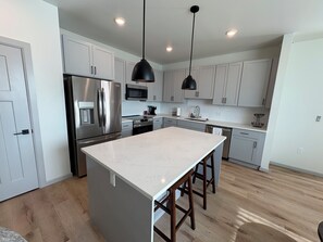 A modern kitchen with stainless steel appliances, a marble countertop, and wooden stools.