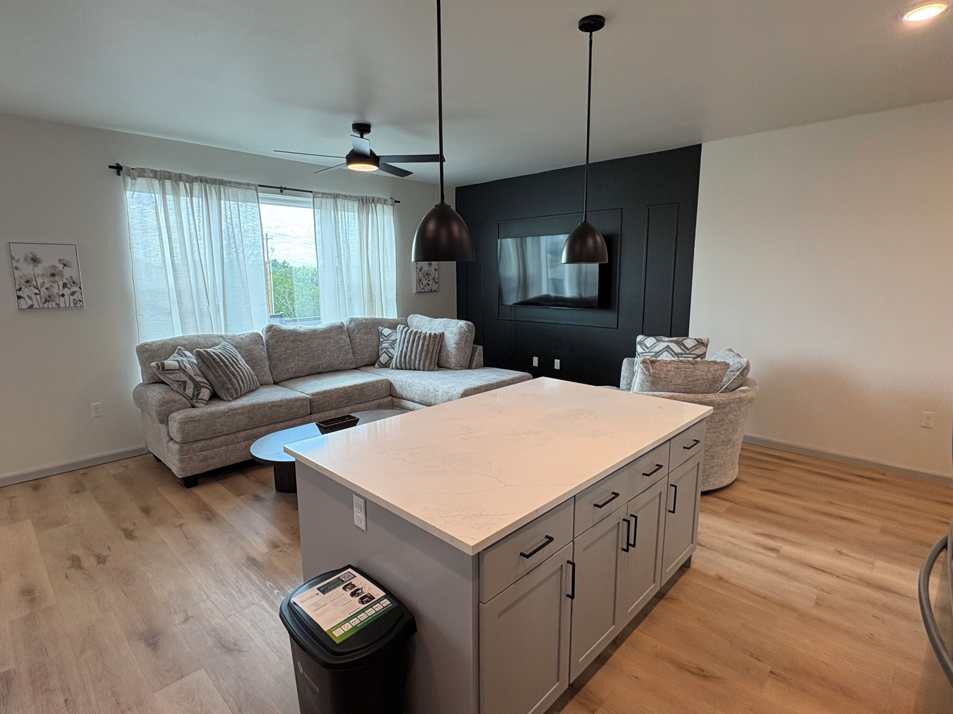 Ett modernt kök med en köksö i mitten, en matplats med en soffa och en takfläkt.