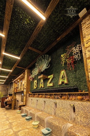 A cozy interior with a green wall, wooden beams, and a seating area with cushions. - BazaHotel&Spa (Mil)