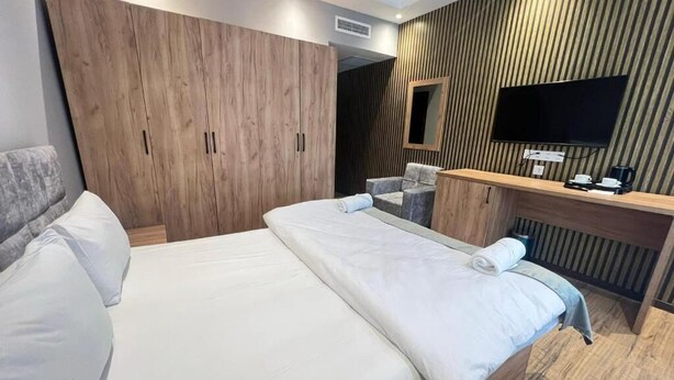 A hotel room with a large bed, wooden wardrobe, a desk with a flat-screen TV, and a seating area. - BazaHotel&Spa (Mil)