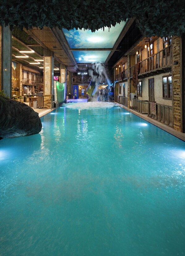 An indoor pool with a waterfall feature, surrounded by rustic wooden walls and a ceiling with a leaf motif.