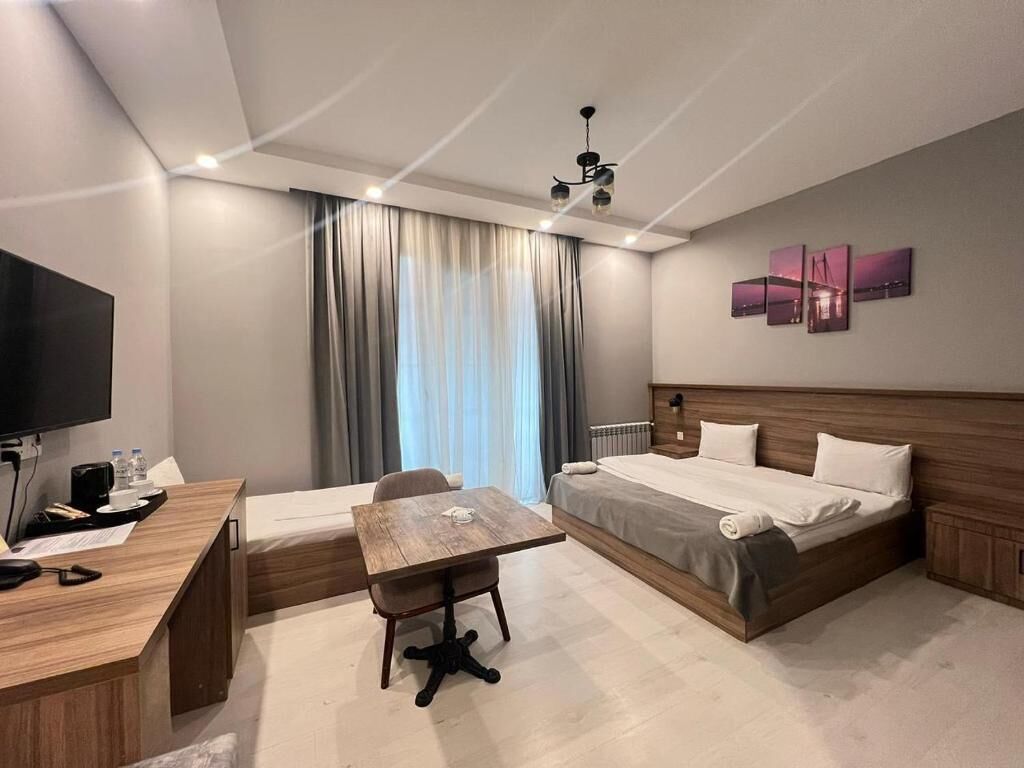Una camera d'albergo con un letto, una scrivania, una sedia, una TV e una finestra con tende.