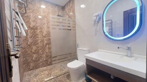 A bathroom with a marble floor, a white sink, a mirror with a blue light, and a shower area. - BazaHotel&Spa (Mil)
