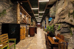 A narrow corridor with wooden benches and tables, a wooden barrel, and a wall with a rocky texture. - BazaHotel&Spa (Mil)