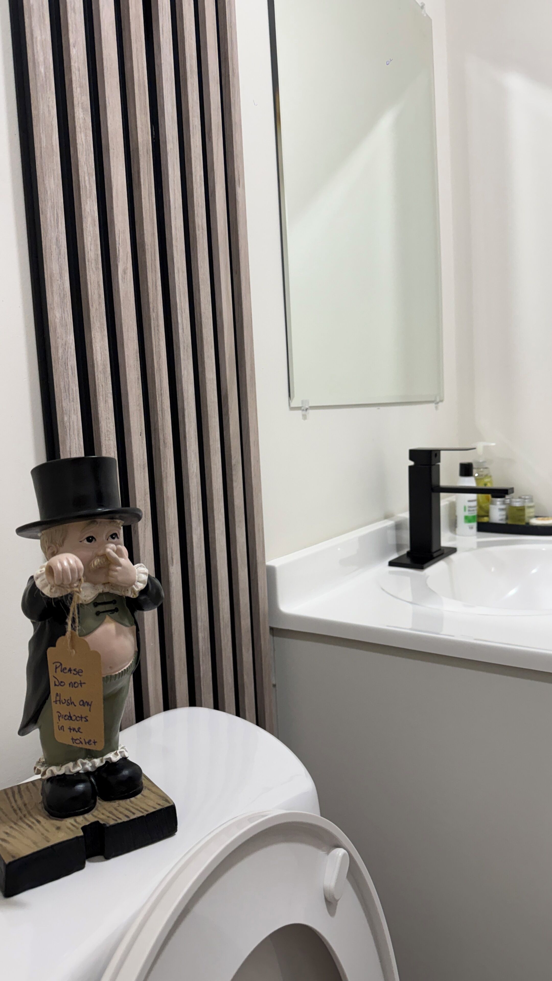 A toilet with a figurine on top and a sign attached to it.