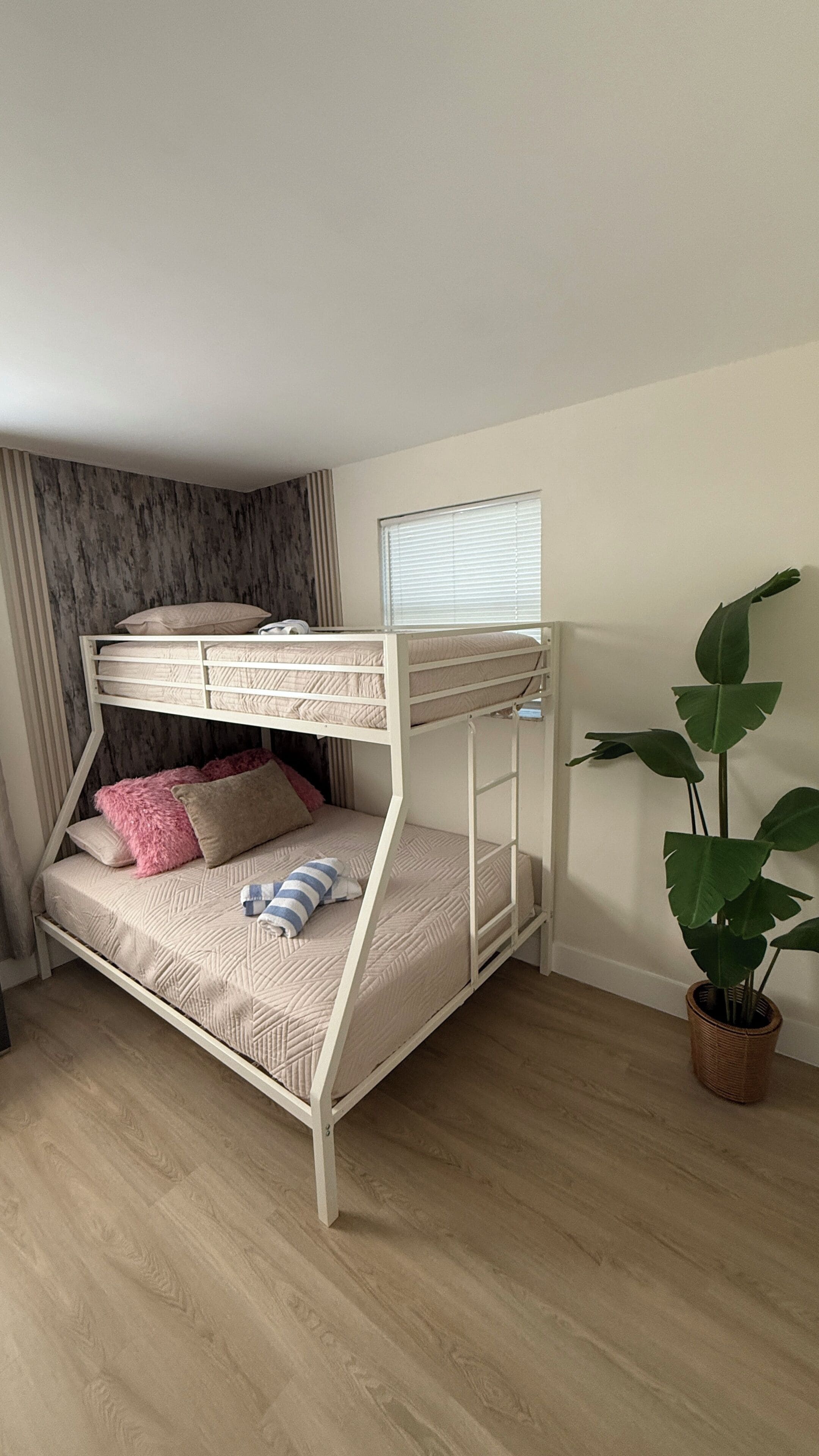 A bunk bed with a window, a potted plant, and a wooden floor.