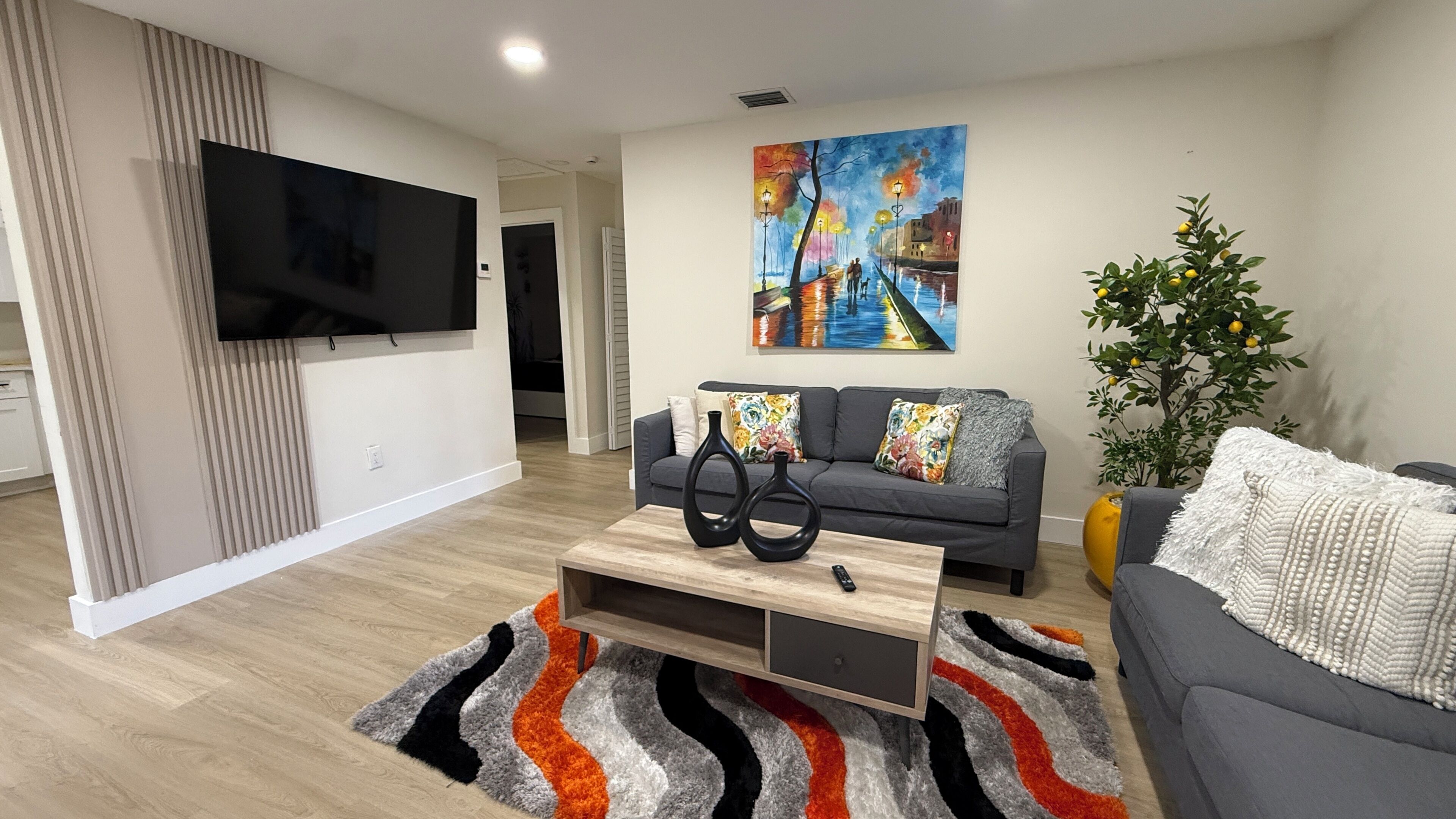 A modern living room with a flat-screen TV, a sofa, a coffee table, and a painting on the wall.