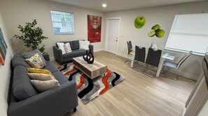 Un salon moderne avec un canapé gris, une table basse et un coin repas comprenant une table en verre et des chaises noires.