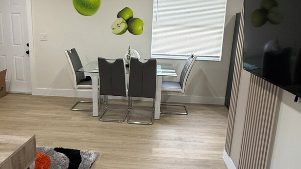 Uma sala de estar moderna com área de jantar, uma TV de tela plana na parede e uma janela com persianas.