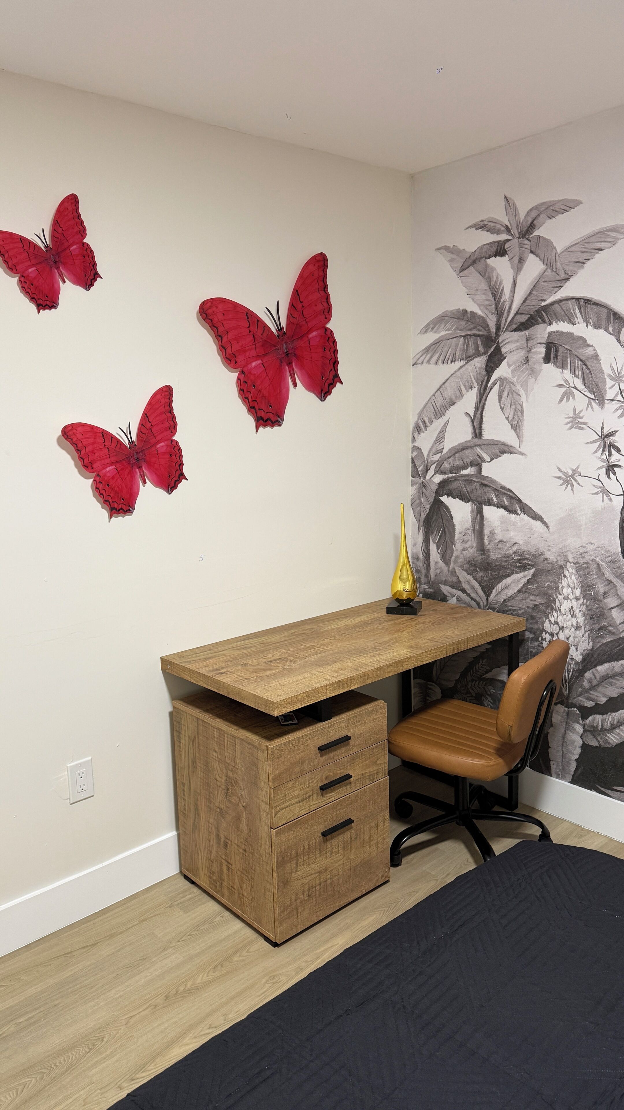 A room with a wooden desk, a chair, and a wall with butterfly decals.