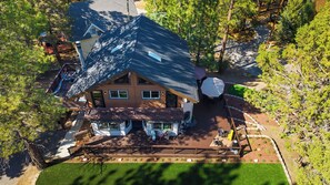 A two-story house with a deck, a garage, and a yard with trees. - Balboa Big Bear by Avantstay Hot Tub + Game Room + Firepit + Putting Green Near Bear Mountain (Big Bear Lake)