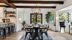 A dining area with a wooden table and chairs, a hanging light fixture, and a view through a window. - Balboa Big Bear by Avantstay Hot Tub + Game Room + Firepit + Putting Green Near Bear Mountain (Big Bear Lake)