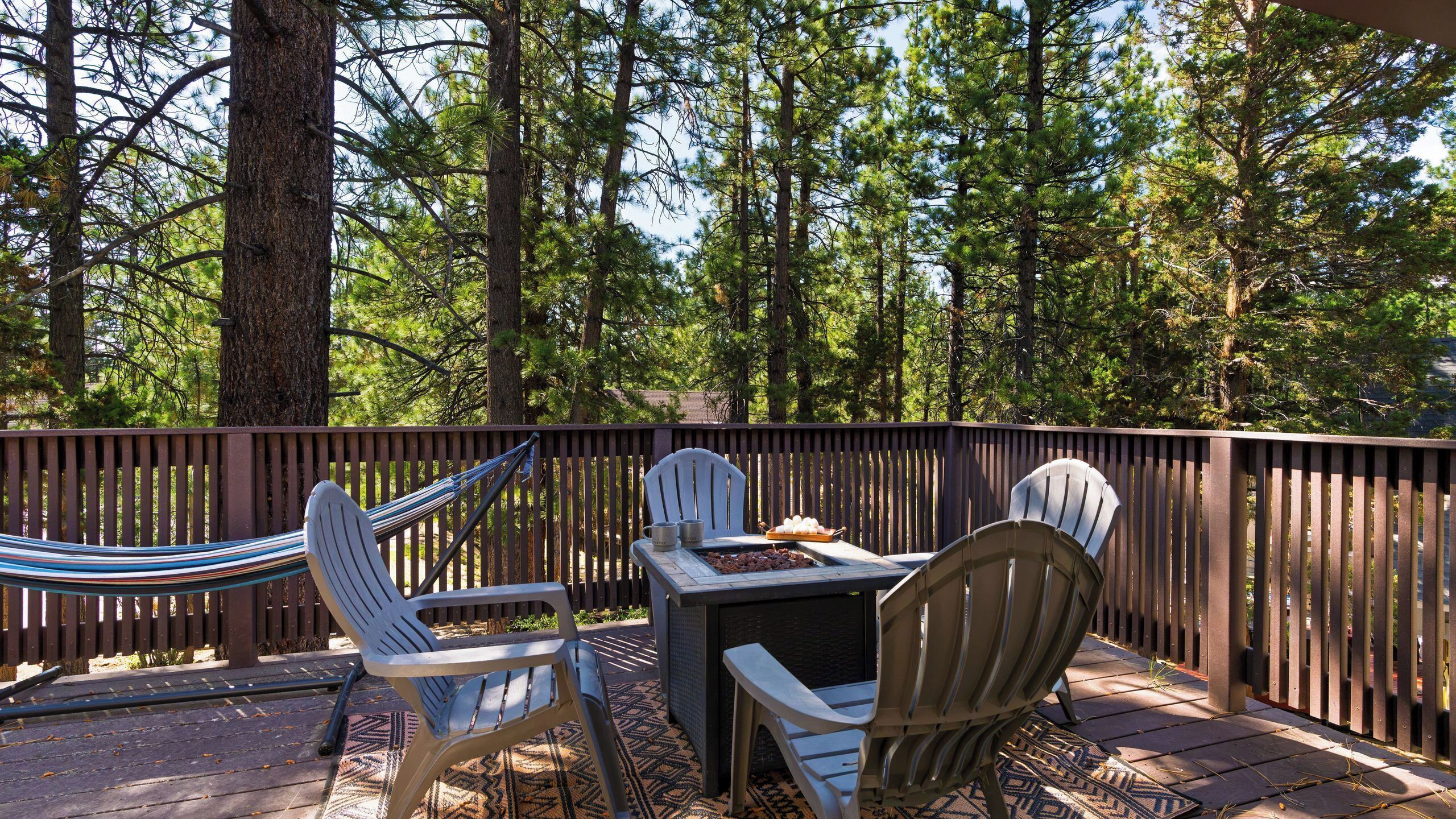An outdoor deck with a table and chairs, surrounded by a wooden fence and tall trees.