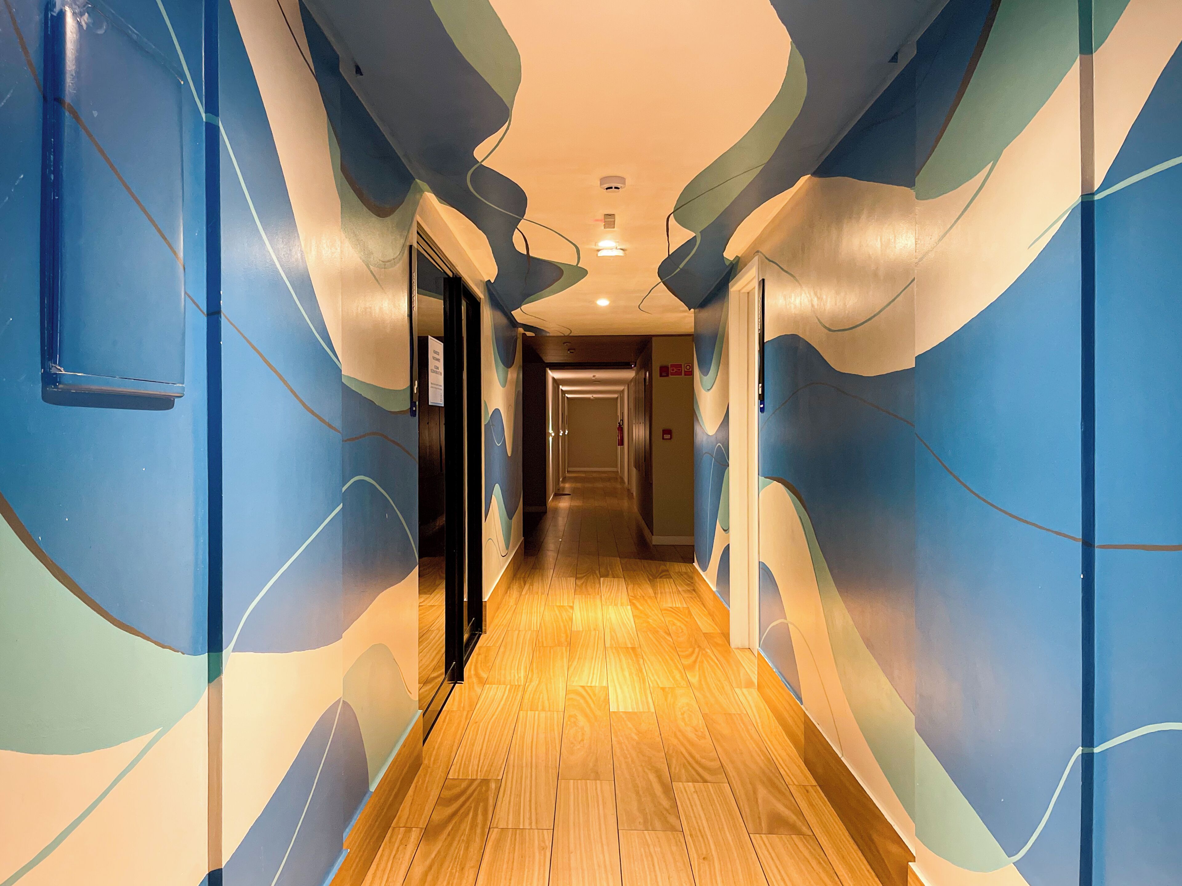 A hallway with a wooden floor and walls painted with abstract blue and green patterns.