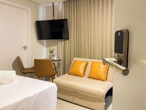 Habitación de hotel con cama, sofá, televisión montada en la pared y un minibar.