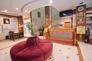 Eine Hotelhalle mit einer Rezeption, einer roten Lounge und einer Treppe zu einer weiteren Etage.