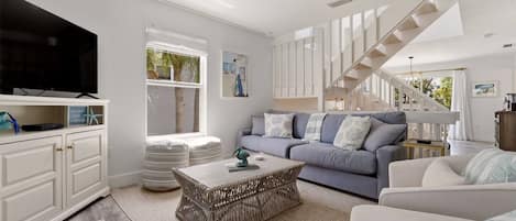 A modern living room with a flat-screen TV, a sofa set, a coffee table, and a staircase.