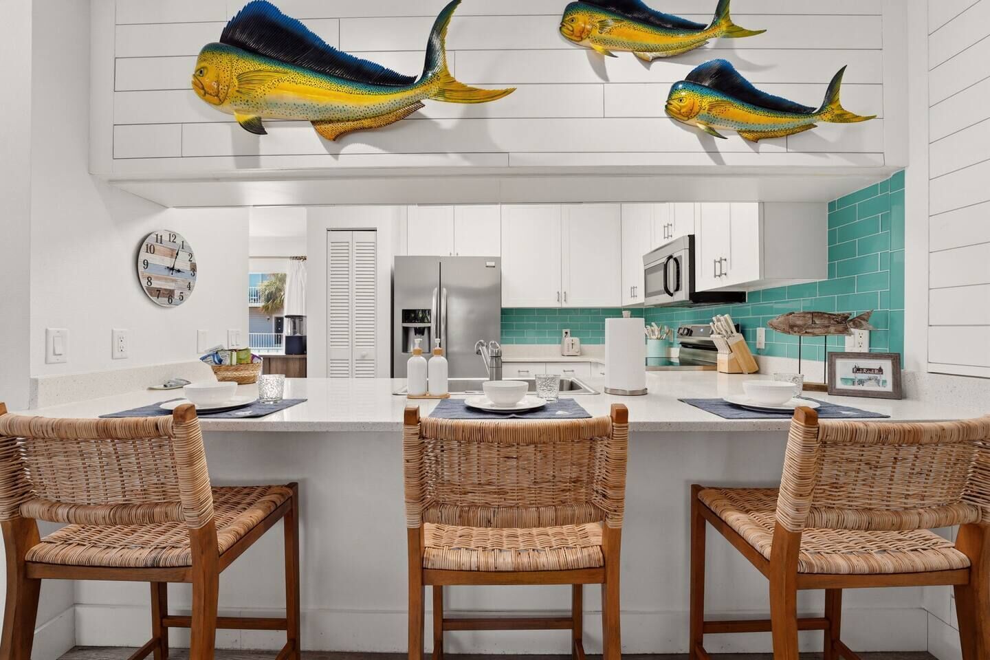 A modern kitchen with white cabinetry, a central island with bar stools, decorative fish wall art, and a teal backsplash.
