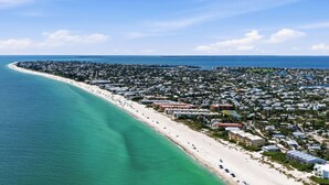Luftaufnahme einer Küstenstadt mit einem langen Sandstrand, dicht bebauten Wohngebieten und blauem Himmel.