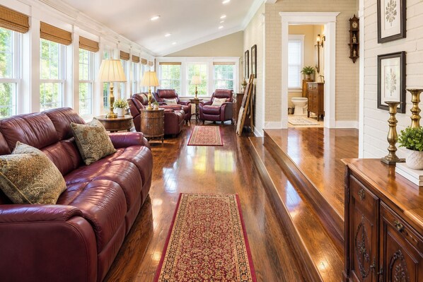 A spacious living room with a leather sofa, wooden flooring, and a view of the adjacent bathroom.
